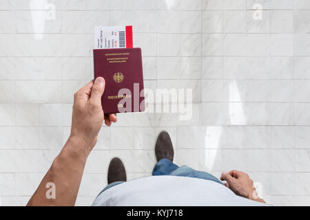 Elevated View Of Male's Hand Holding Passport And Boarding Pass Standing On Floor Stock Photo