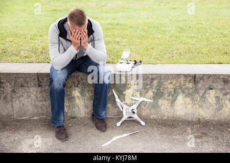 Young Worried Man With Broken Drone Sitting In The Park Stock Photo