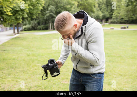 Young Man With Nausea Holding Virtual Reality Headset In The Park Stock Photo