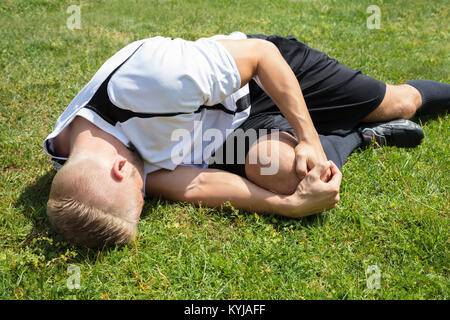 Close-up Of Male Player Suffering From Knee Injury Lying On Field Stock Photo