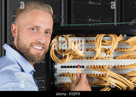 Portrait Of A Smiling Young Computer Technician Checking The Server Cables In Data Center Stock Photo