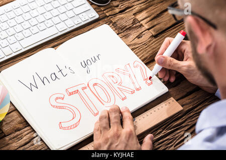 Elevated View Of Businessman Asking What's Your Story On Notebook Over The Office Desk Stock Photo