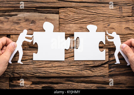 Close-up Of Hands Joining The Two White Jigsaw Pushed By The Two Figures Stock Photo