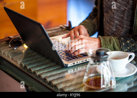 Caucasian man's hands type on laptop  with coffee mug and coffee cup next to him in a coffee shop with focus on keyboard Stock Photo