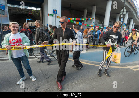 Class War protesters walk across Cable Street at the protest against the Jack the Ripper museum holding yellow tape with the message 'Crime Scene - Do Not Enter'. Stock Photo