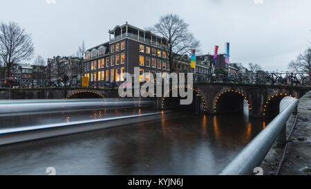 River cruise passing through under a canal bridge in Amsterdam during dusk Stock Photo