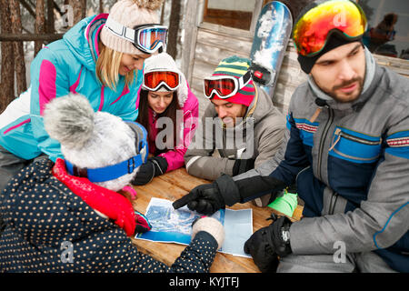 smiling friends looking at map in the snow on a cold winter day Stock Photo