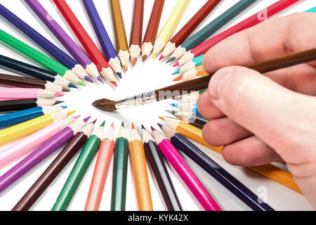 Man hand with a brush paints the heart laid out from colored pencils, isolated on white background Stock Photo