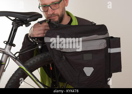 Bearded man inserts bike carrier bag on rear rack of mtb bicycle. Stock Photo