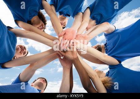 Happy Multiracial Janitors Stacking Hands Against Cloudy Sky Stock Photo