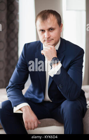 Man the groom in suit sitting on sofa in hotel Stock Photo