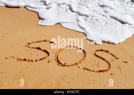 SOS message written in the sand with a wave coming in.. Stock Photo