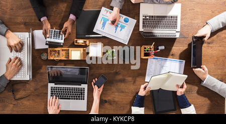 Overhead View Of Businesspeople Hands On Office Desk Using Electronic Devices Stock Photo