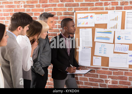 Business Colleague Looking At Graph Attached On Bulletin Board Over The Brick Wall Stock Photo