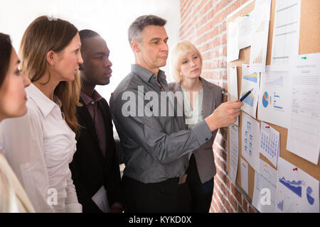 Mature Manager Analyzing The Graph With His Colleague Attached On Bulletin Board Stock Photo