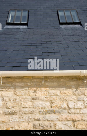 Two rooflights in a slate tiled roof above a limestone wall Stock Photo