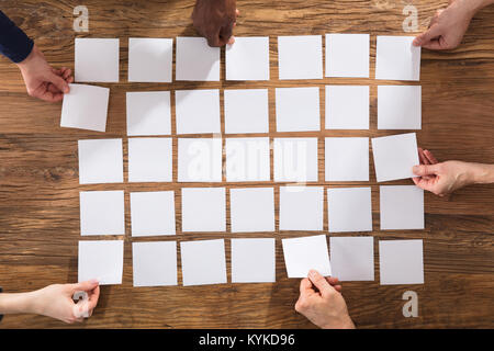 Overhead View Of People Hands Arranging White Papers On Wooden Table Stock Photo
