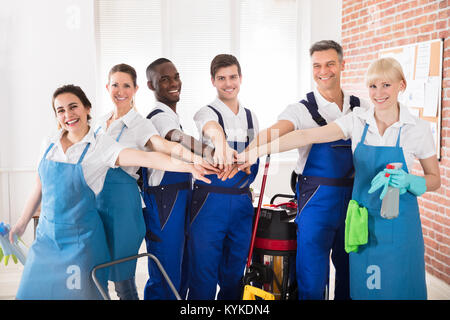Portrait Of Happy Diverse Janitors In The Office With Cleaning Equipments Stacking Hands Stock Photo