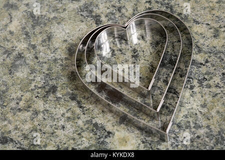 A set of three heart shaped cookie cutters on a marble effect kitchen surface Stock Photo