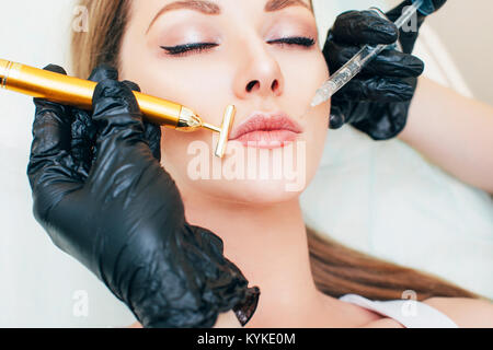 Close up of hands of cosmetologist making botox injection in female lips. She is holding syringe. The young beautiful woman is receiving procedure wit Stock Photo