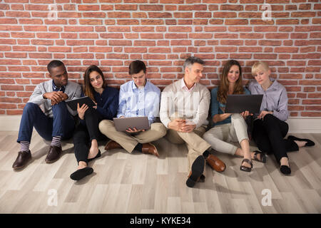 Row Of Diverse Businesspeople Sitting On Hardwood Floor Using Laptops And Digital Tablets Stock Photo
