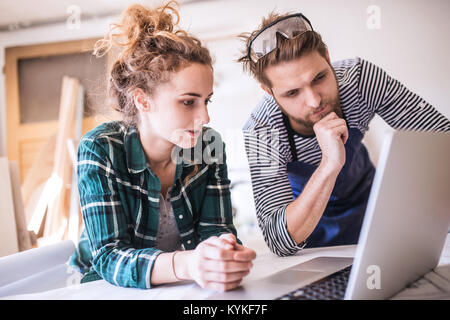 Young couple with laptop in the carpenter workroom. Stock Photo