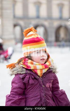 Paris little girl wears a colorful winter hat and scarf set and a purple coat outdoors on a cold January day. French fashion for children Stock Photo