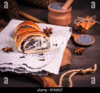 poppy roll on a gray linen napkin and poppy seeds in a wooden spoon, close up Stock Photo