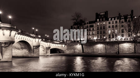 Paris illuminated bridge and buildings at night with reflections in the Seine River. Black and white sepia toned Stock Photo