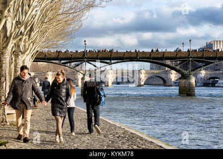 Paris, France, couples walk under old trees along the Seine River. Above is seen the famous bridge covered with love locks, which were later removed. Stock Photo