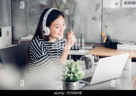 Young asian casual businesswoman arm on desk rest pose with laptop computer and listening music via headphone and think about work ,work at home with  Stock Photo