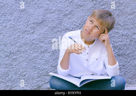 Kid reading, writing and thinking sitting on the ground and doing his school homework. Stock Photo