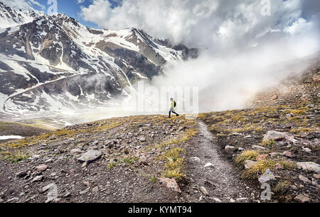 Hiker in green shirt with backpack walking in the snowy mountains at foggy sky background Stock Photo