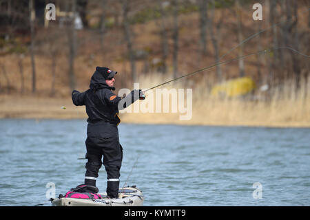 Parainen, Finland - April 20, 2017: Finnish fisherman casting pike fishing fly while standing on a special fishing kayak on an overcast spring day in  Stock Photo