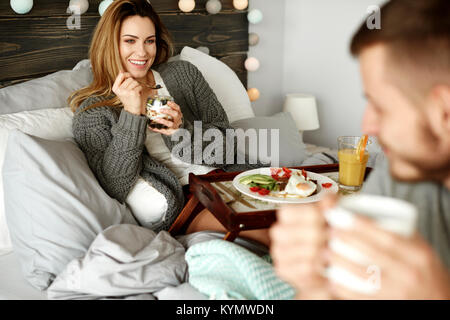 Cheerful woman eating in bed Stock Photo