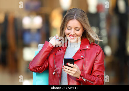 Front view portrait of a happy shopper shopping and using a smart phone in a mall Stock Photo