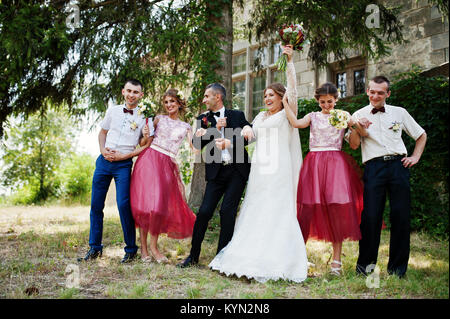 Bridesmaids with groomsmen and wedding couple jumping, dancing and having fun next to an old building. Stock Photo
