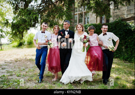 Bridesmaids with groomsmen and wedding couple jumping, dancing and having fun next to an old building. Stock Photo