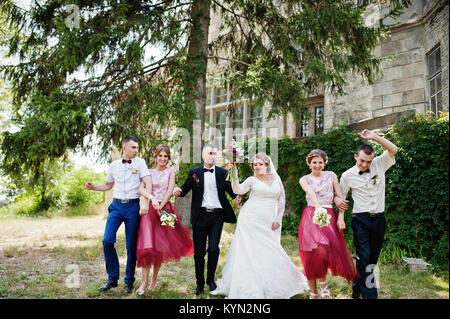 Bridesmaids with groomsmen and wedding couple jumping, dancing and having fun next to an old building. Stock Photo