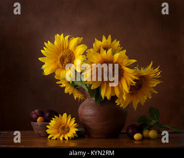Bouquet of sunflowers in old clay jug.  In the foreground branches with ripe cherry plum Stock Photo