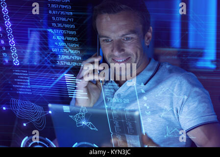 Positive man talking on the phone and smiling while holding a tablet Stock Photo