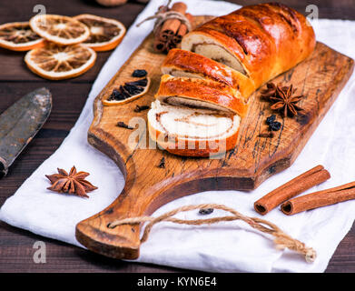 baked roll with cinnamon and nuts on a brown wooden board, close up Stock Photo