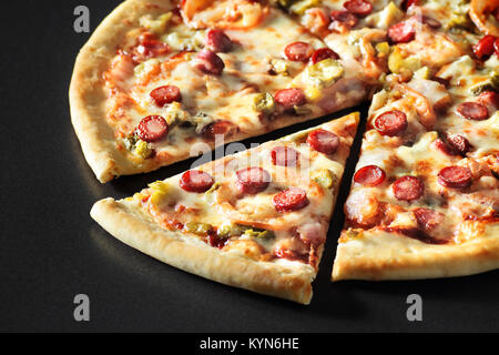 cut Pizza close up with sausages on black stone background Stock Photo