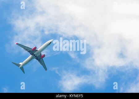 Unidentifiable Airplane flying over head with bright blue sky heading towards white clouds. Stock Photo