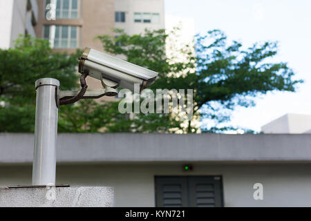 Grey CCTV camera mounted on top of a wall watching over an area. Stock Photo
