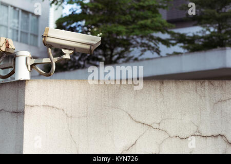 Grey CCTV camera mounted on top of a wall watching over an area. Stock Photo