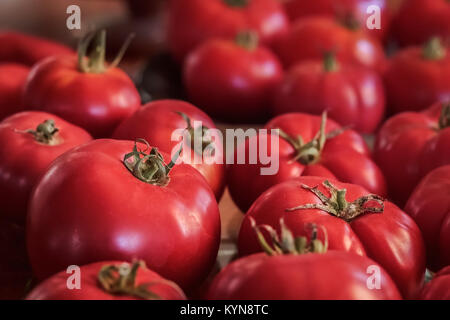 Ripe, red, organic, homegrown heritage variety tomatoes fill the frame, with side lighting and selective focus on two near the front of the image. Stock Photo