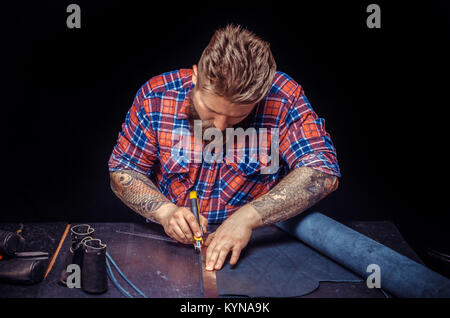 Craftsman performing leatherwork on a new product piece in the workplace Stock Photo
