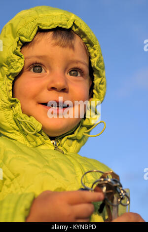 Portrait of little girl child with keys in sunny autumn evening, sunset sunlight. On the clear blue sky background Stock Photo