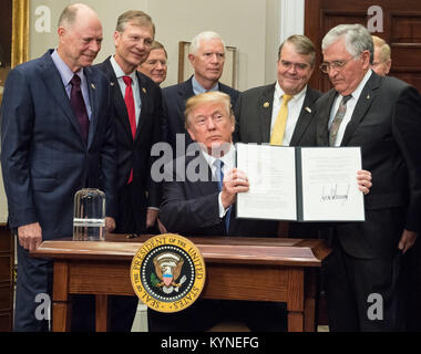 President Donald Trump holds up the Space Policy Directive - 1 after signing it, directing NASA to return to the moon, alongside members of the Senate, Congress, NASA, and commercial space companies in the Roosevelt room of the White House in Washington, Monday, Dec. 11, 2017. Photo Credit: (NASA/Aubrey Gemignani) Stock Photo